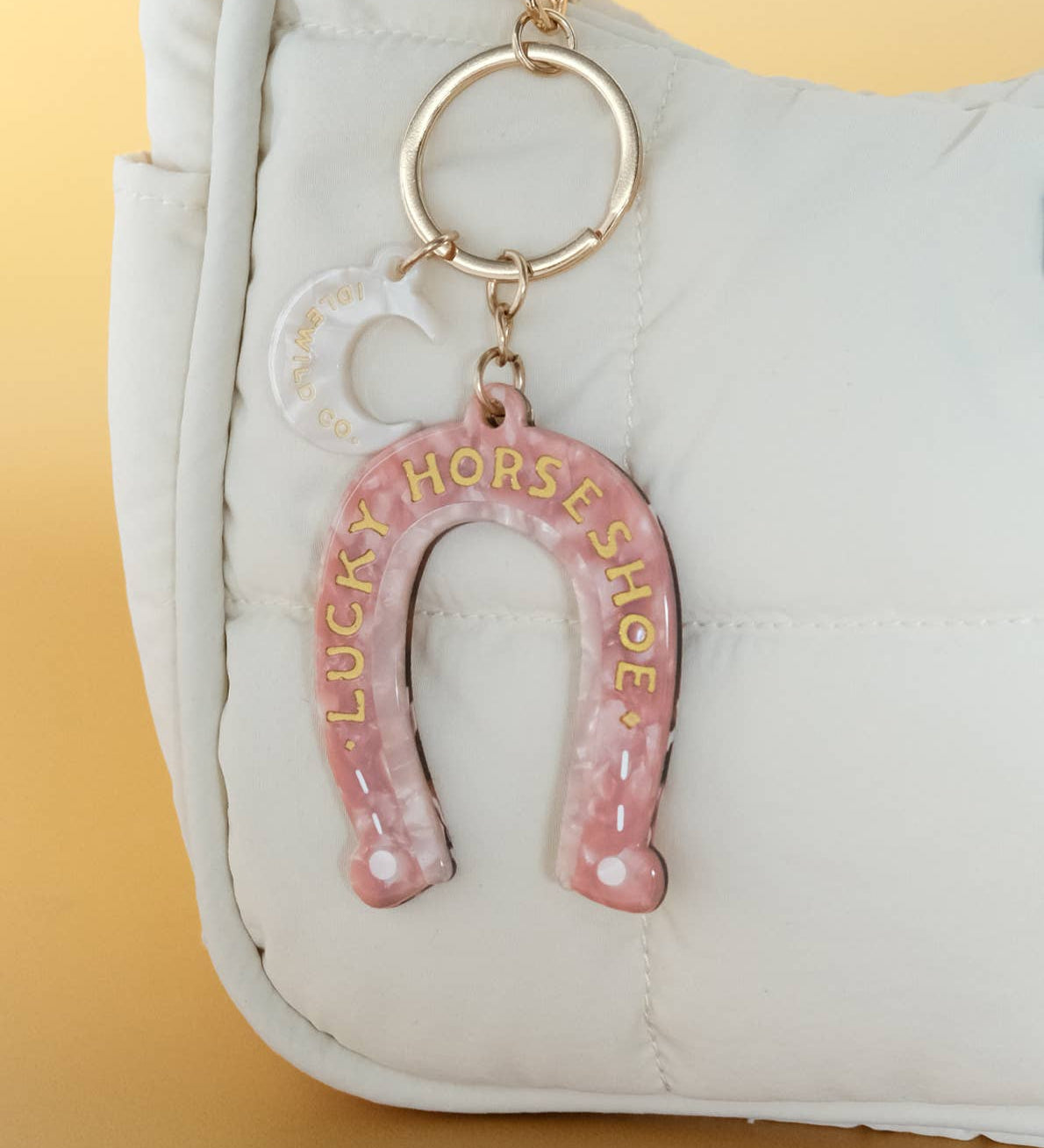 Pink horseshoe keychain with 'Lucky Horseshoe' text on a white bag against a yellow background