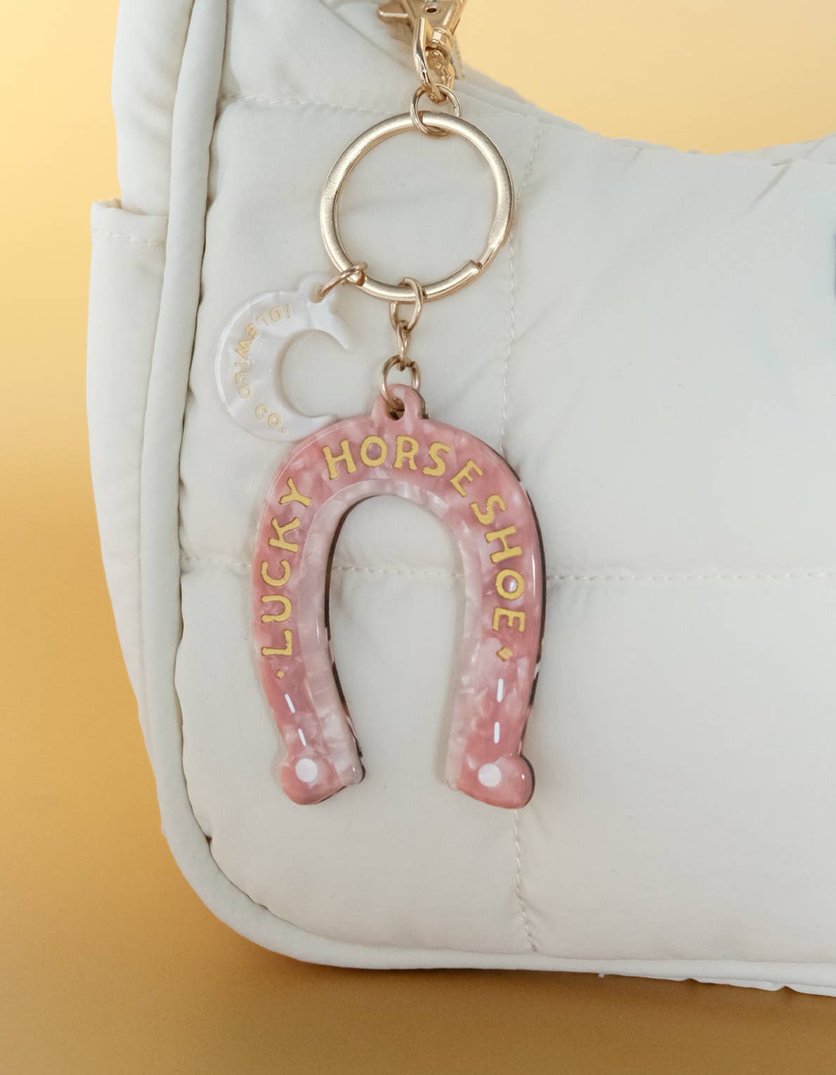 Pink horseshoe keychain with 'Lucky Horseshoe' text on a white bag against a yellow background