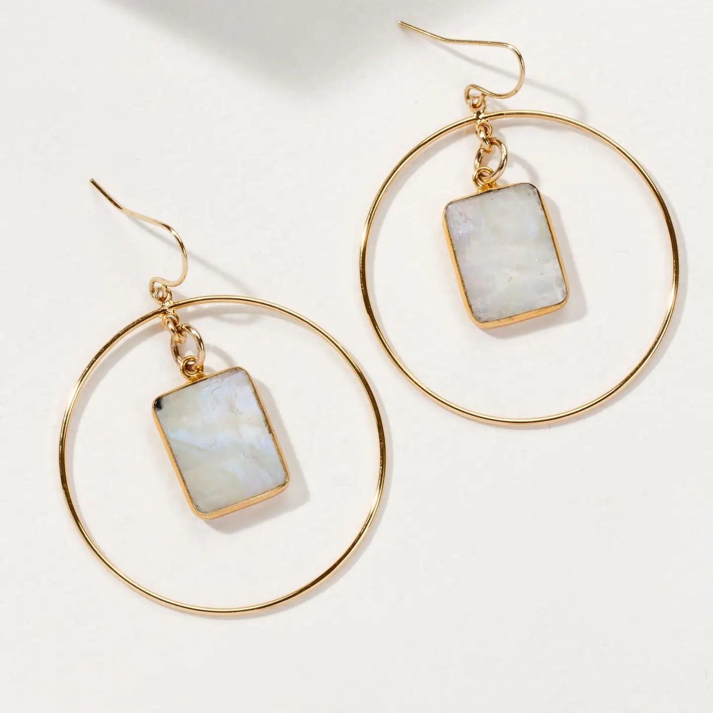 Gold hoop earrings with rectangular moonstone pendants in center, on a white background