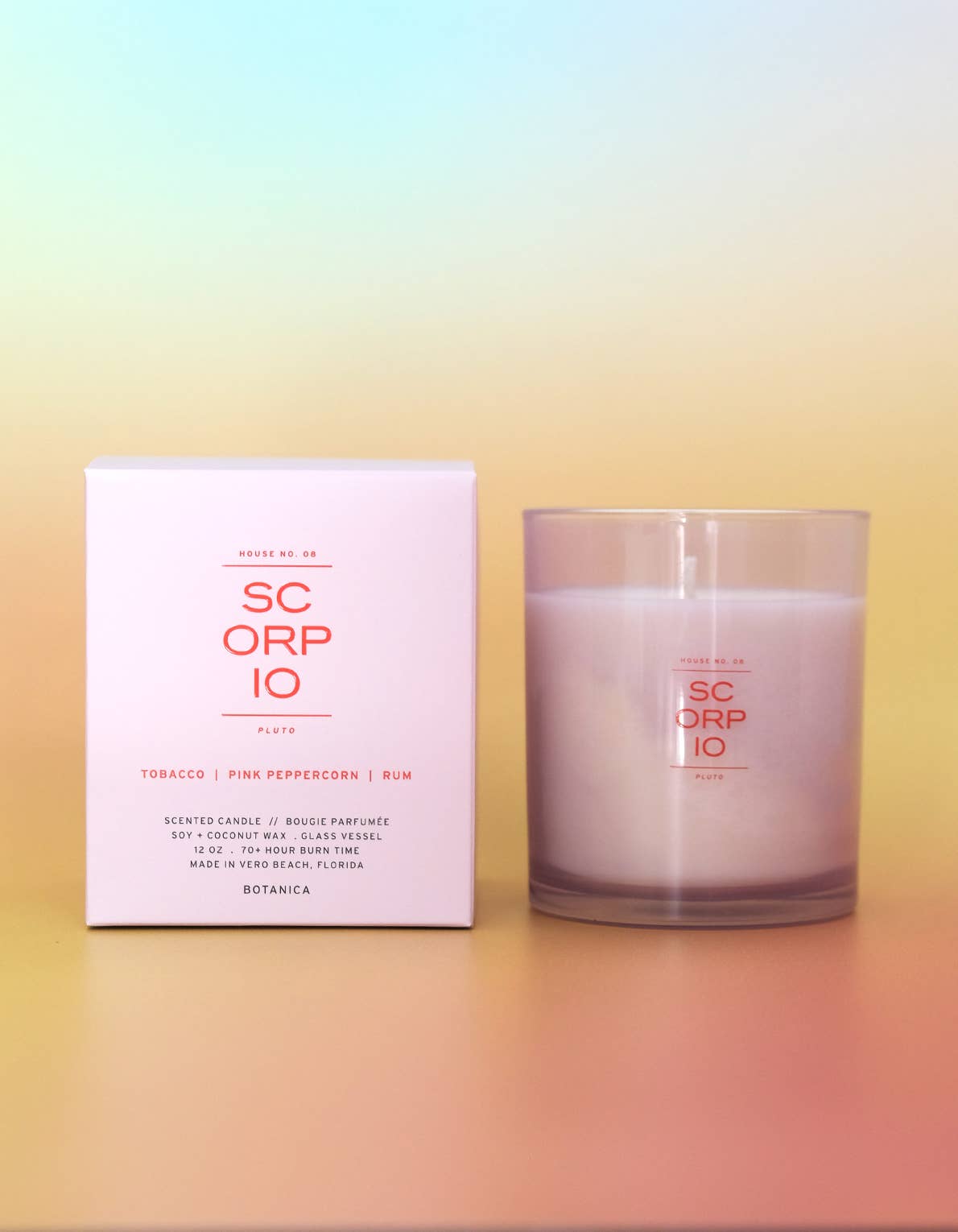 A SC ORP IO scented candle in a frosted glass jar next to its white packaging box, featuring pink and orange text, set against a pastel gradient background.