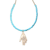 Necklace with turquoise beads and a hand pendant on a textured green surface.