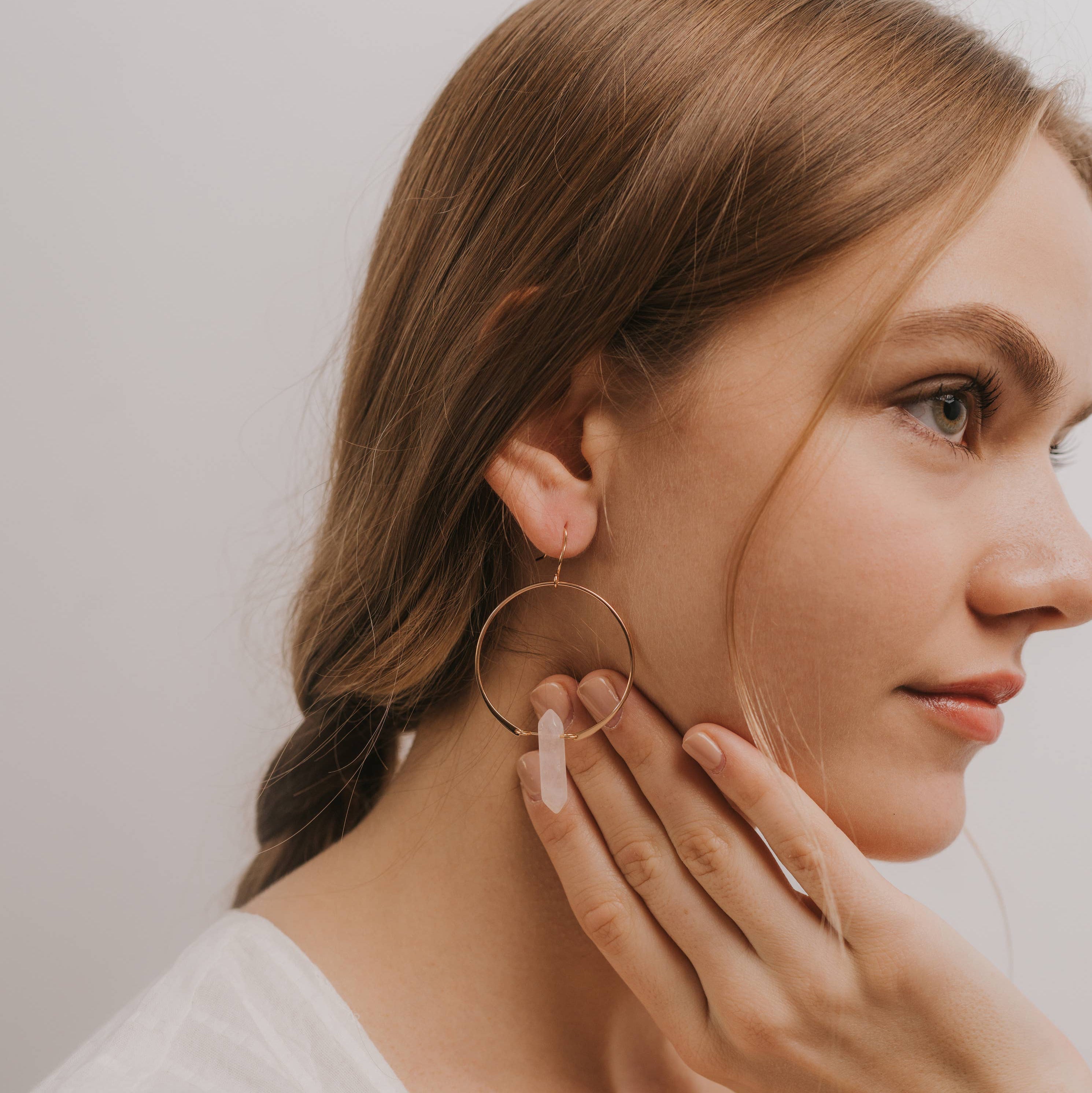 Woman wearing gold hoop earrings and a ring, with a neutral background