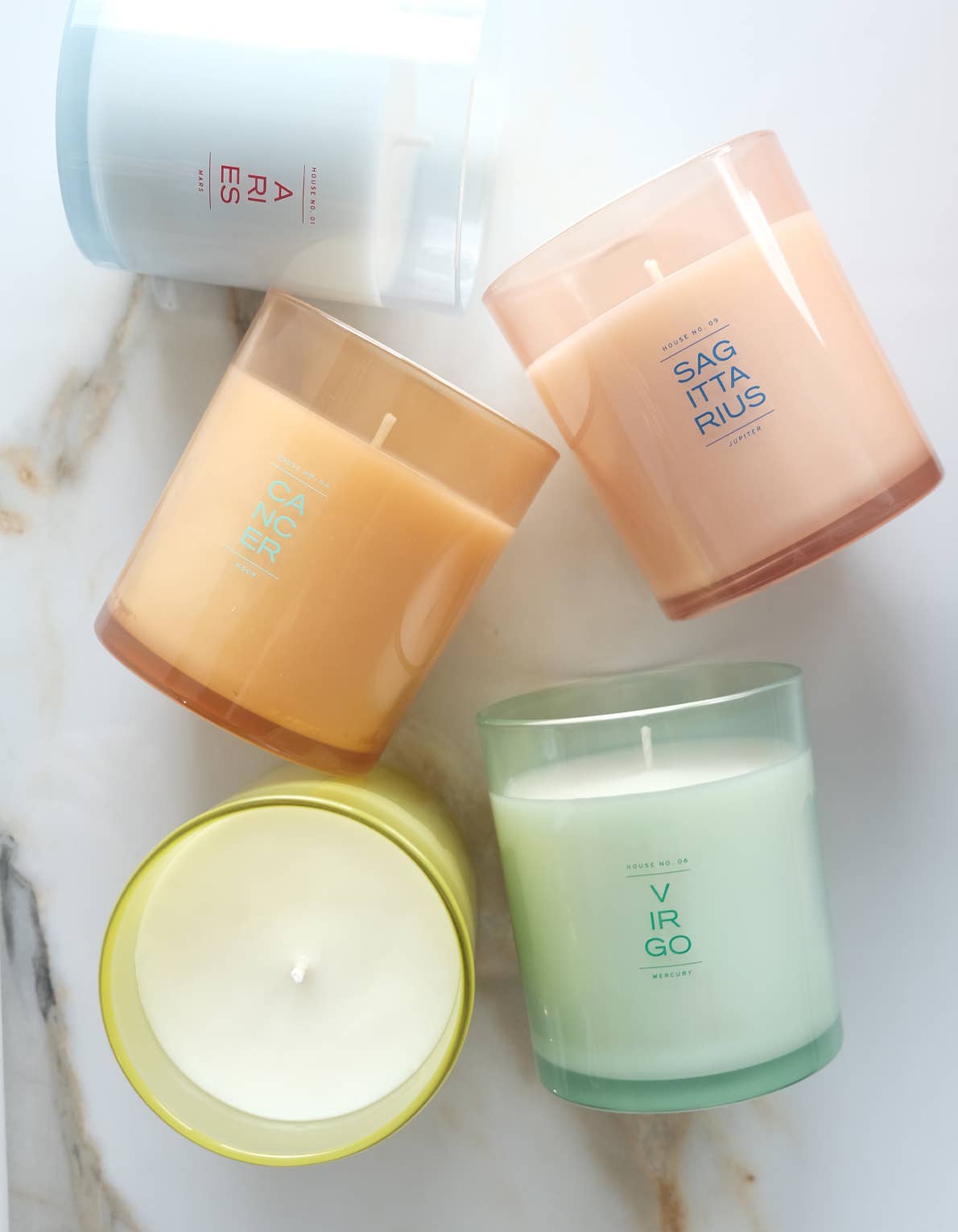 Four candles with zodiac-themed labels on a marble surface