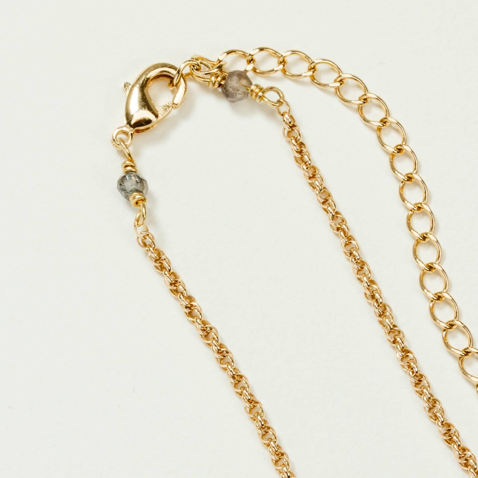 Gold necklace chain with a clasp and small grey stones on either side, resting on a white background