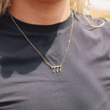 Person wearing a necklace with a minimalistic design on a plain background