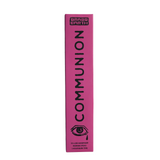 A tall, narrow pink box for Brass Earth Communion skincare stands vertically against a white background. The box features black text reading 'BRASS EARTH COMMUNION' and a black eye illustration near the bottom.