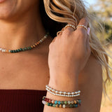 Close-up of a woman's arm wearing multiple beaded bracelets with a blurred natural background