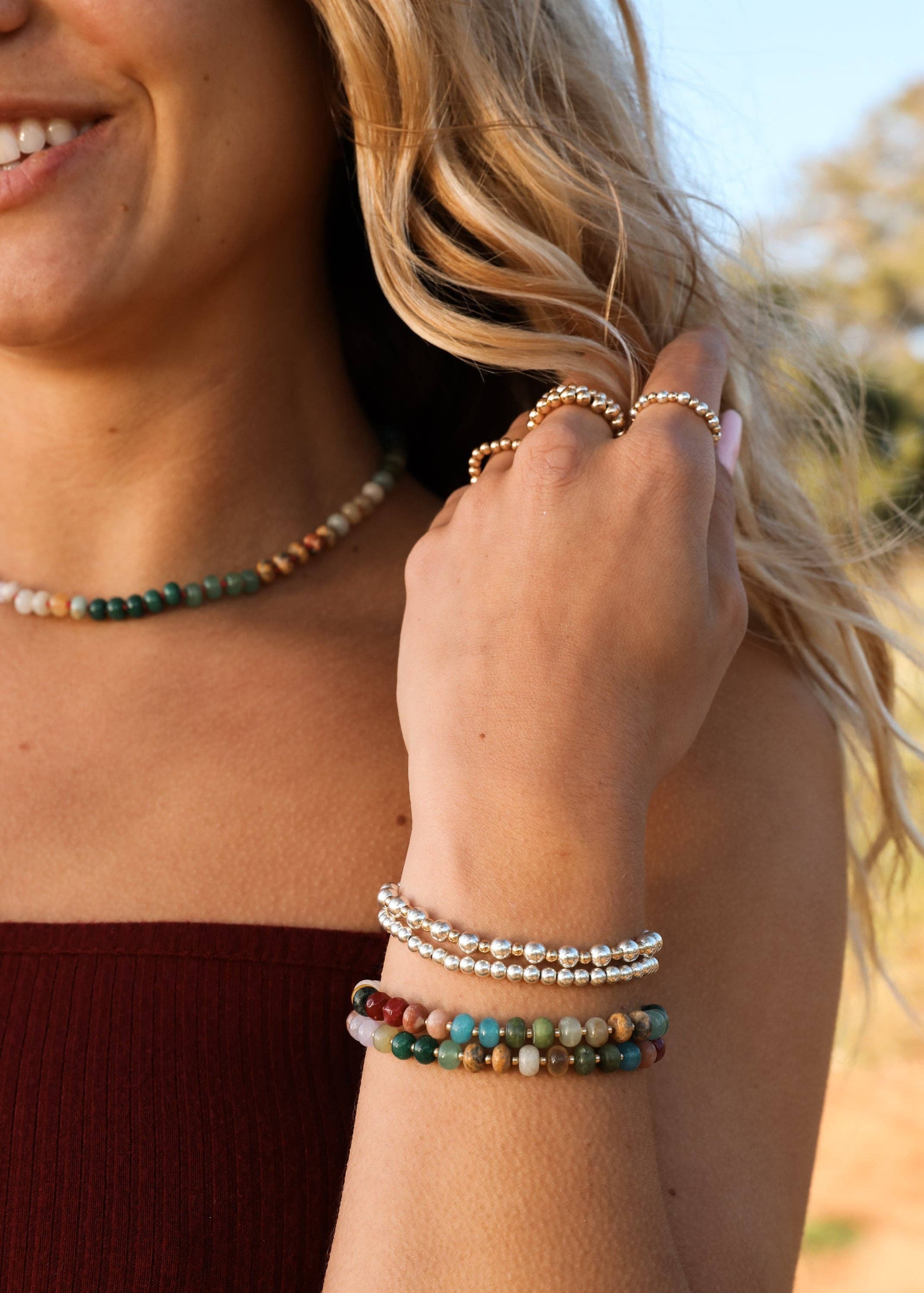 Close-up of a woman's arm wearing multiple beaded bracelets with a blurred natural background