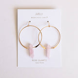 Gold hoop earrings with rose quartz stones on a Jaxxelly branded card.
