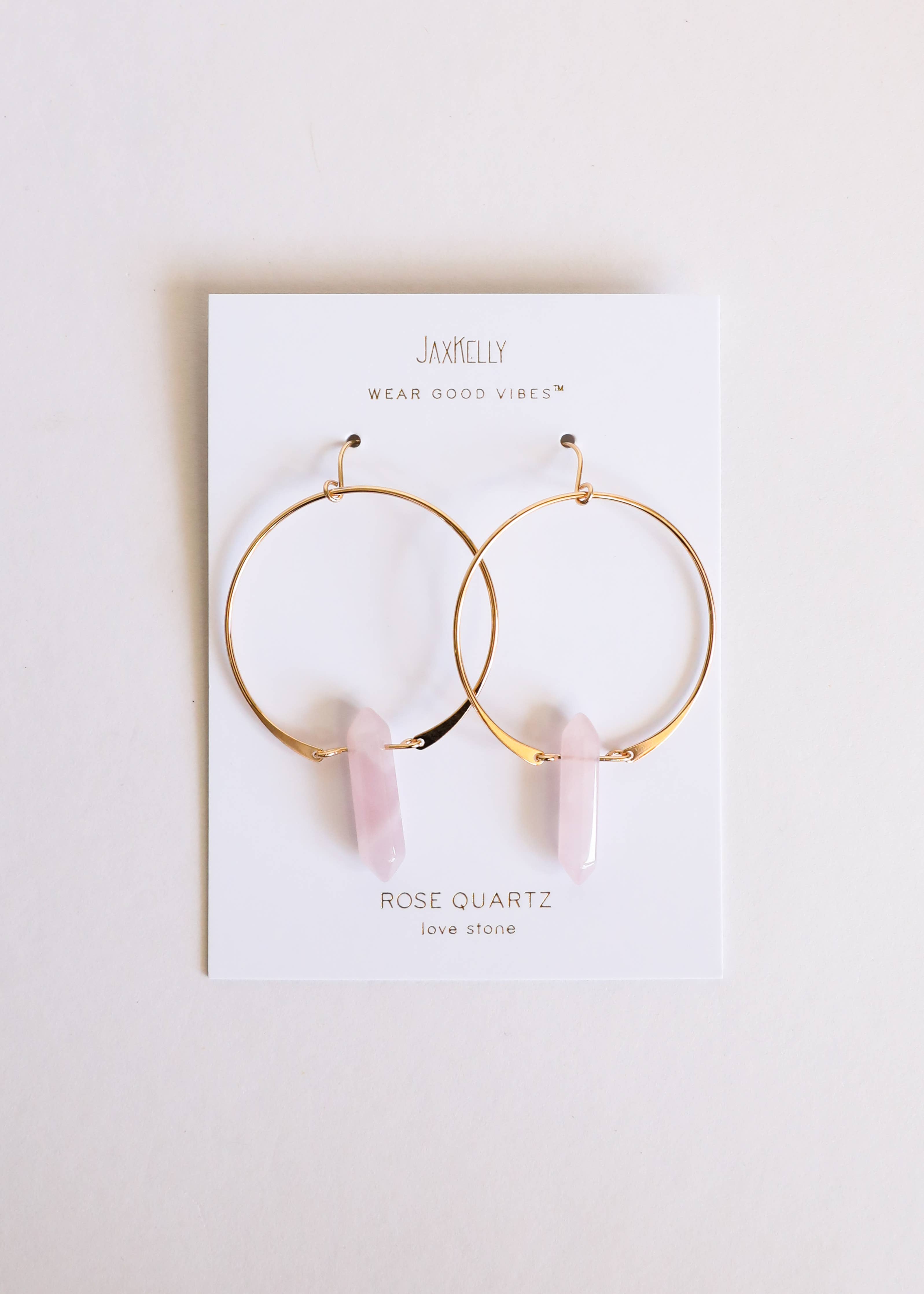 Gold hoop earrings with rose quartz stones on a Jaxxelly branded card.