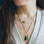 Close-up of a woman wearing layered necklaces with green gemstones.