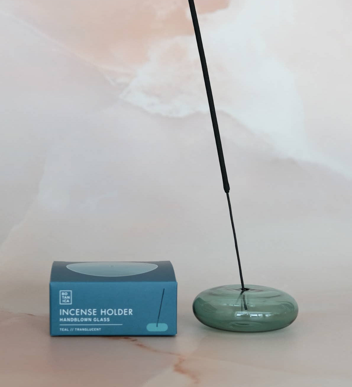 Green incense holder with a single stick of incense next to its packaging on a light background