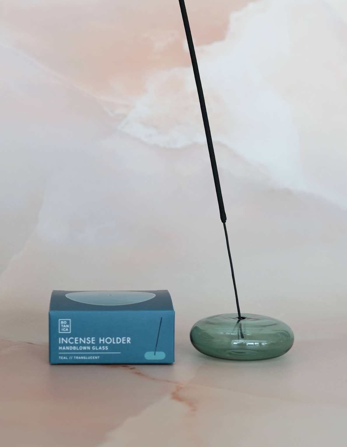 Green incense holder with a single stick of incense next to its packaging on a light background