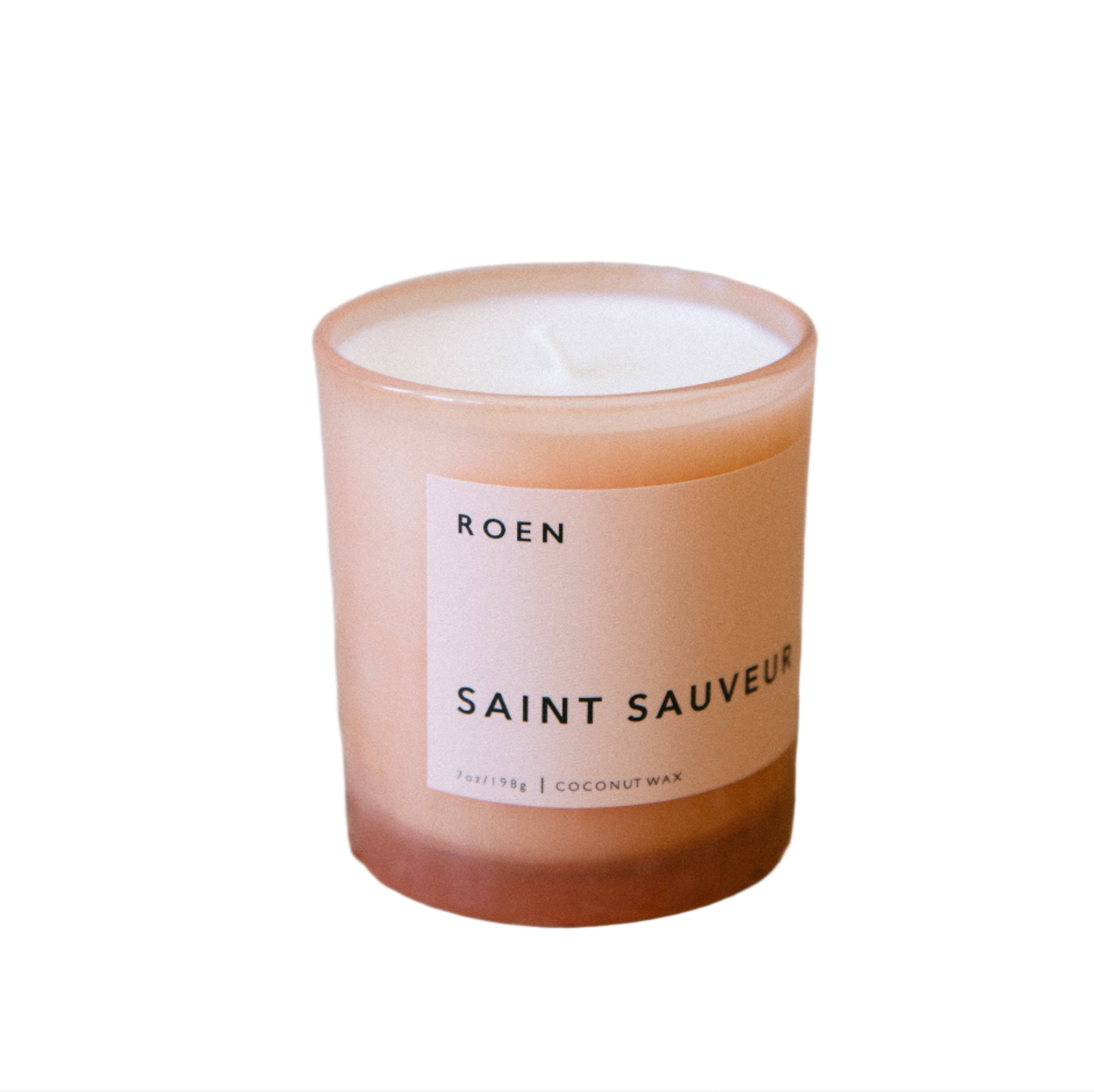 A beige candle with a white label that reads 'ROEN SAINT SAUVEUR' on the front, set against a plain background.