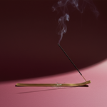 Incense stick with smoke on a pink surface against a dark background