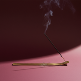 Incense stick with smoke on a pink surface against a dark background