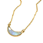 Gold necklace with a crescent moon shaped moonstone pendant on a light background