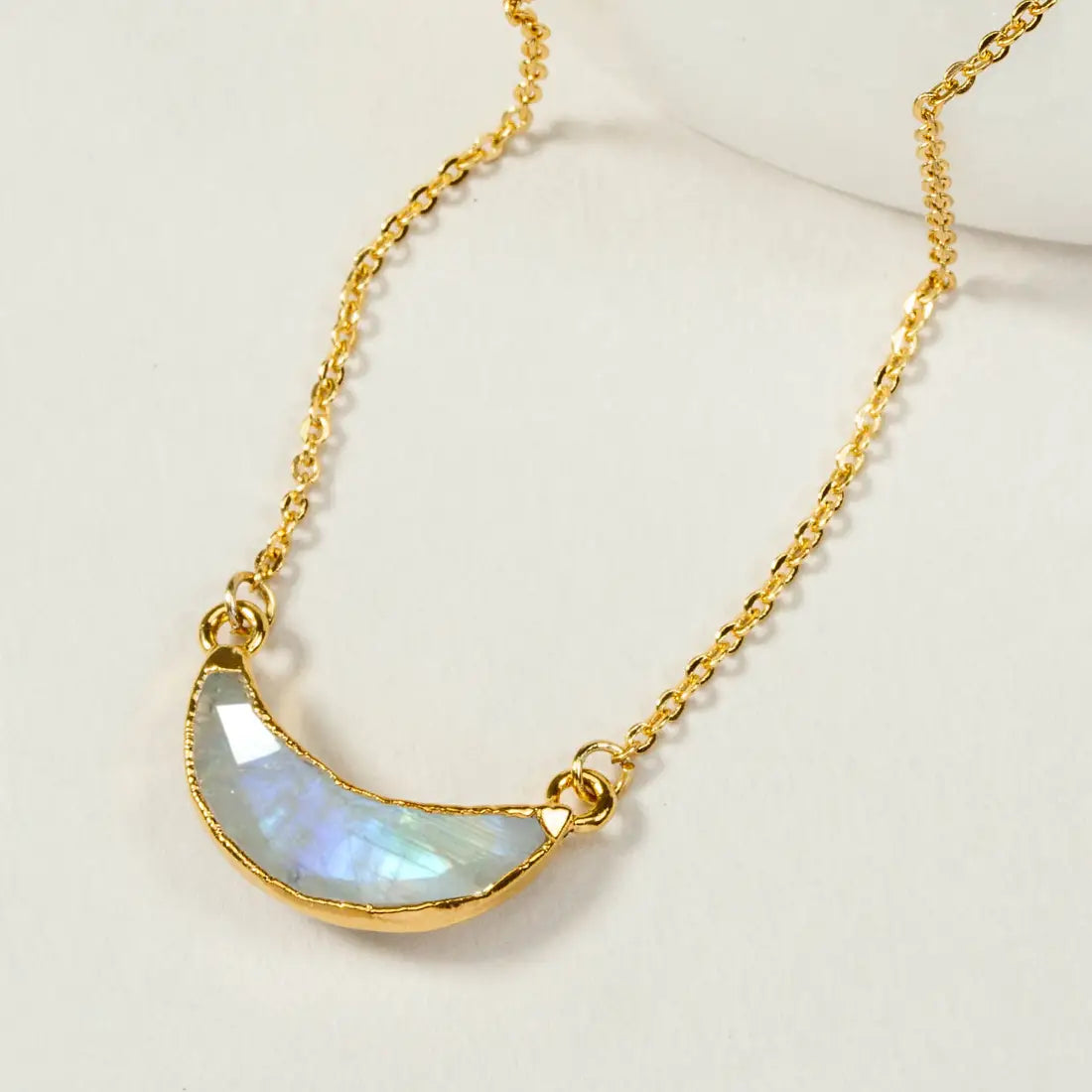 Gold necklace with an upward facing crescent moon moonstone pendant, displayed on a light background