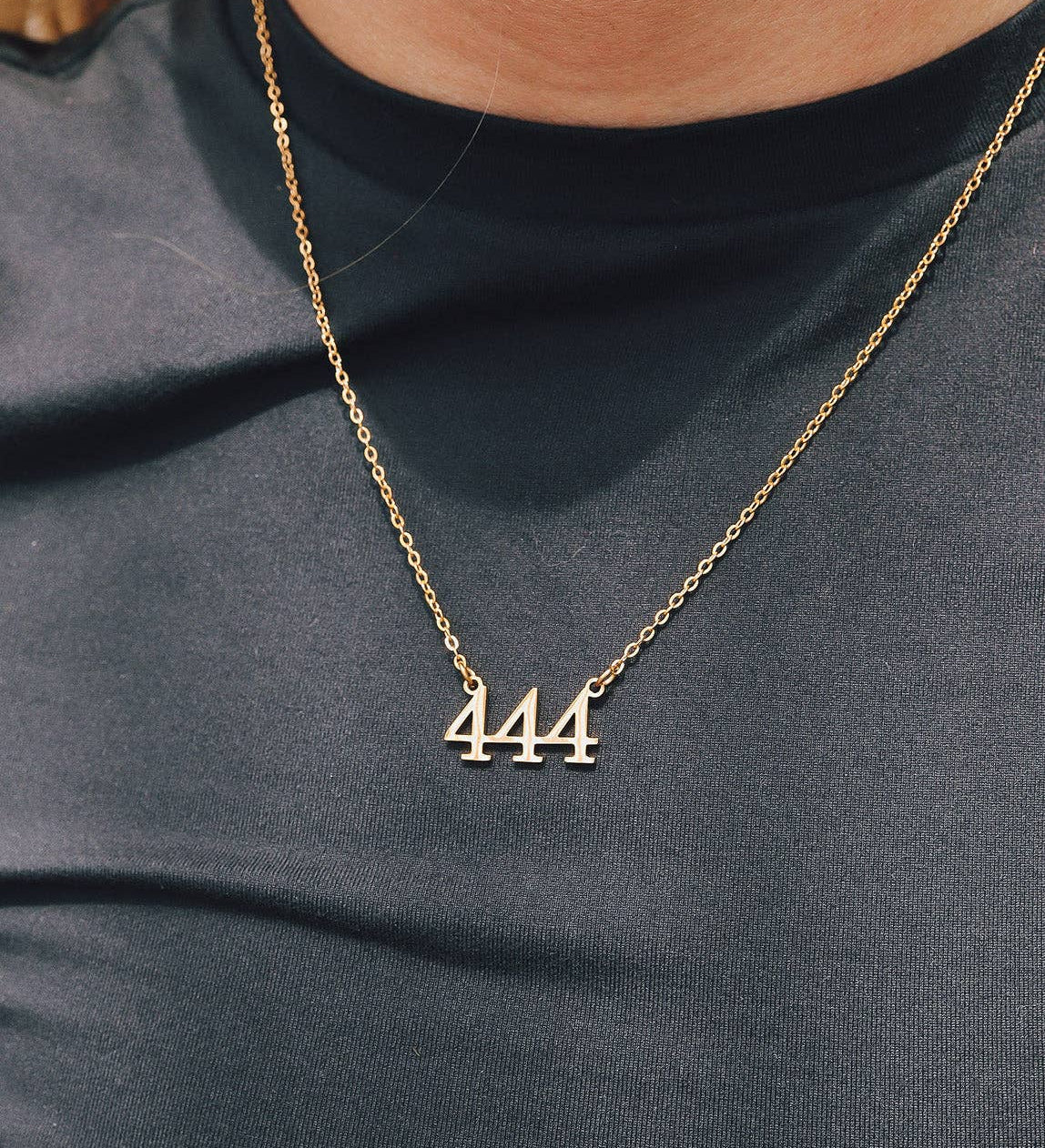 Gold necklace with '444' pendant on a person wearing a dark shirt