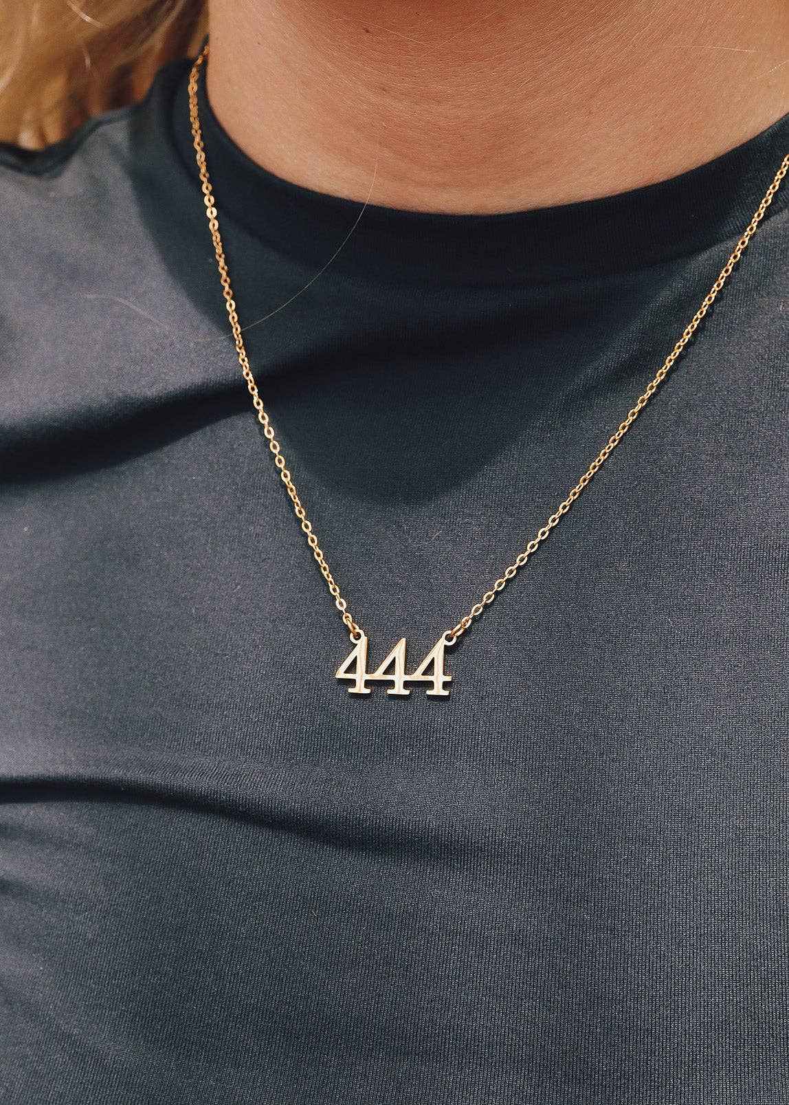 Gold necklace with '444' pendant on a person wearing a dark shirt