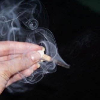 Hand holding a lit palo Santo wood match with smoke against a dark background